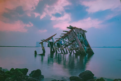 Abandoned wooden post in sea against sky