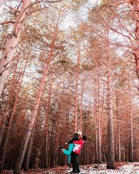 Side view of man picking up girlfriend in forest during winter