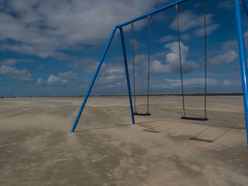 View of swing on beach against cloudy sky