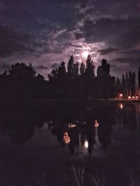 Silhouette trees by lake against sky at night