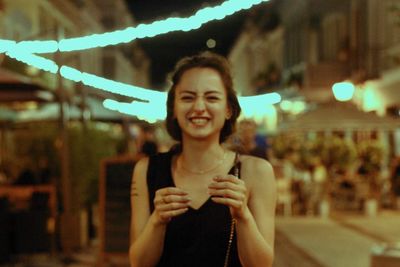 Portrait of young woman holding camera at night