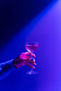 Hand holding elegant glass with an alcoholic cocktail. alcoholic drink in neon lights