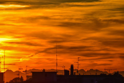 Silhouette factory against orange sky