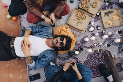 Directly above shot of man lying down by friends sitting on picnic blanket during party