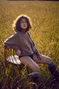  portrait  woman in a sweater and shorts sitting on a field on a wood vintage chair in autumn