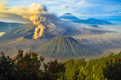 Scenic view of volcanic mountains erupting ashes against sky