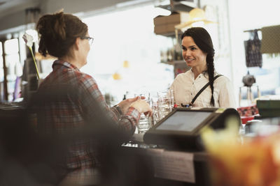 Owner showing drinking glasses to customer while standing at checkout counter in store