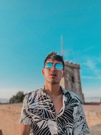 Portrait of young man wearing sunglasses standing against sky