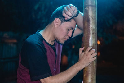 Side view of stressed young man leaning on rod at night