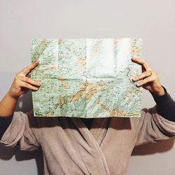 Woman holding map in front of face against wall