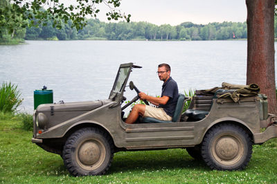 Young man sitting on off-road vehicle on grassy field by lake