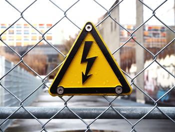 Close-up of high voltage sign board on chainlink fence