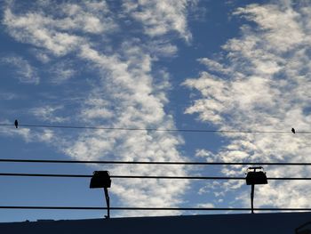 Low angle view of silhouette birds on cable against sky