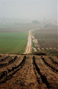 Dirt road passing through field against sky