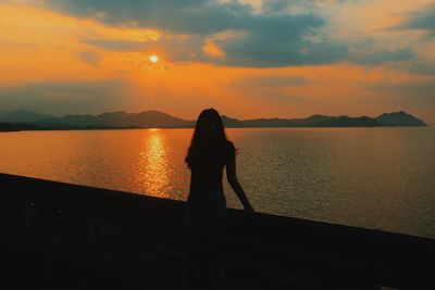 Silhouette man standing by lake against orange sky