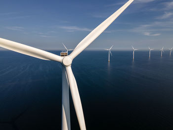 Wind turbines by sea against sky