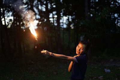 Portrait of woman holding illuminated sparkler on land against trees