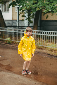 A boy in a yellow raincoat walks outside in the rain. a child jumps on the narrows. 