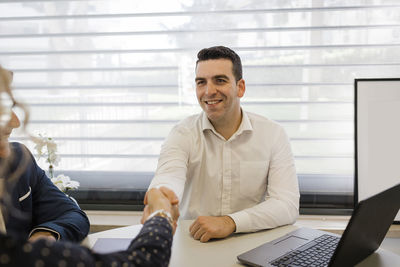 Happy businessman shaking hands with colleague at desk in office