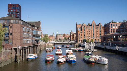 Sailboats in canal amidst buildings against clear sky