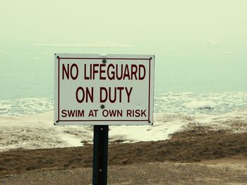 Close-up of signboard by sea against sky