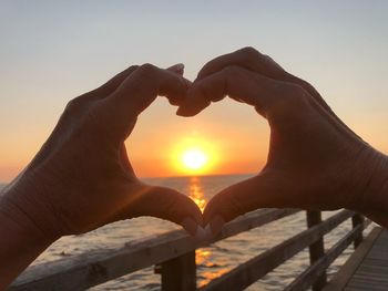 Cropped hands making heart shape against sun during sunset