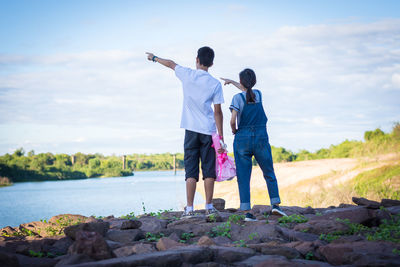 Rear view of men standing on shore against sky