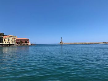 Buildings in sea against clear blue sky