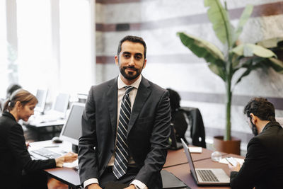 Portrait of bearded businessman sitting on desk in office