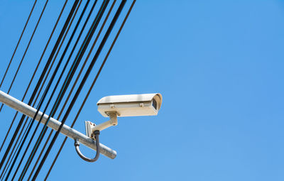 Low angle view of security camera against clear blue sky