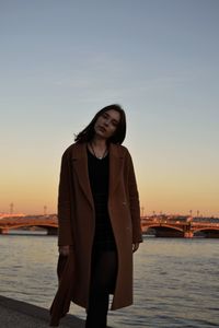 Portrait of smiling young woman standing against sea during sunset