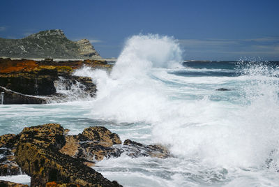 Waves splashing on rocks at shore against sky