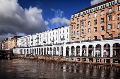 Scenic view of buildings next to river against cloudy sky