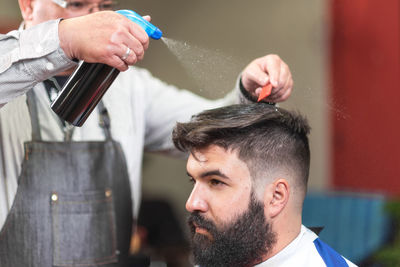 Midsection of barber sprinkling water on male customer hair in salon