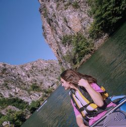 Young woman on rock by tree against clear sky