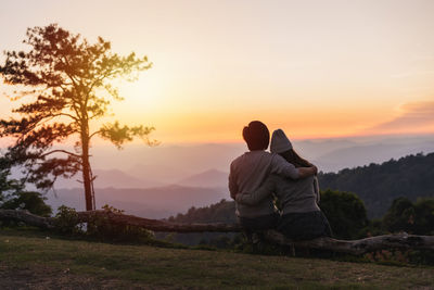 Rear view of couple sitting on mountain against sky at sunset
