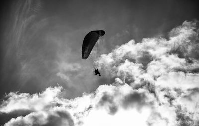 Low angle view of people paragliding against sky