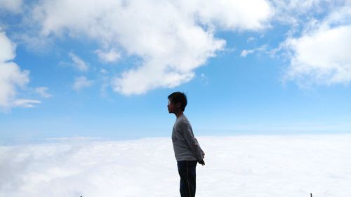 Side view of boy standing against clouds and sky