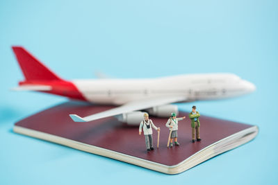 Close-up of hiker figurines on passport with airplane model against blue background