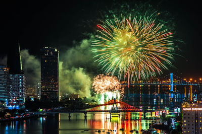 Firework display over illuminated buildings and river in city at night