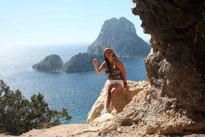 Young woman standing on rock by sea against sky