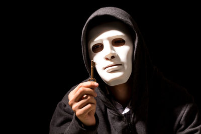 Criminal in mask holding key against black background