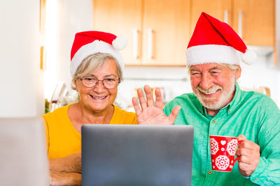 Smiling man with coffee cup waving by woman while video conferencing over laptop