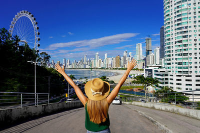 Girl with raised arms on balneario camboriu skyline with ferris wheel, santa catarina, brazil