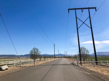 Road by electricity pylon against sky