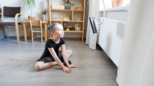 Cute girl looking away while sitting on hardwood floor at home