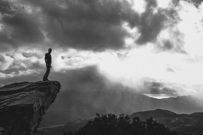 Silhouette man standing on cliff against sky