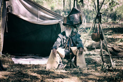 Senior man sitting on seat by camping tent in forest