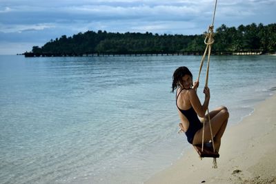 Woman on swing at beach against sky