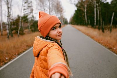 Happy girl in orange hat invites to share with her pleasure of walking through the autumn forest